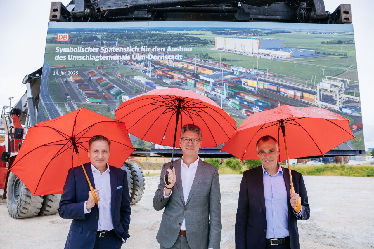 Nebeneinander stehen der Andreas Schulz, Vorsitzender der Geschäftsführung Deutsche Umschlaggesellschaft Schiene-Strasse mbH, Dornstadts Bürgermeister Rainer Braig und DB-Infrastrukturvorstand Berthold Huber mit Regenschirmen in der Hand beim Spatenstich.